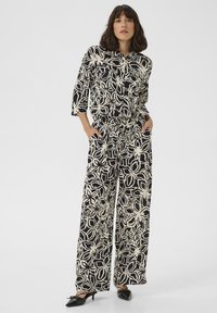 Black and cream floral patterned outfit with a button-up top, relaxed-fit pants, and pockets, featuring a lightweight texture and wide legs.