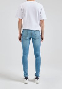 Bílý tričko s krátkým rukávem a světle modré skinny džíny s pěti kapsami. Viditelné prošívání a tenisky s černými akcenty.