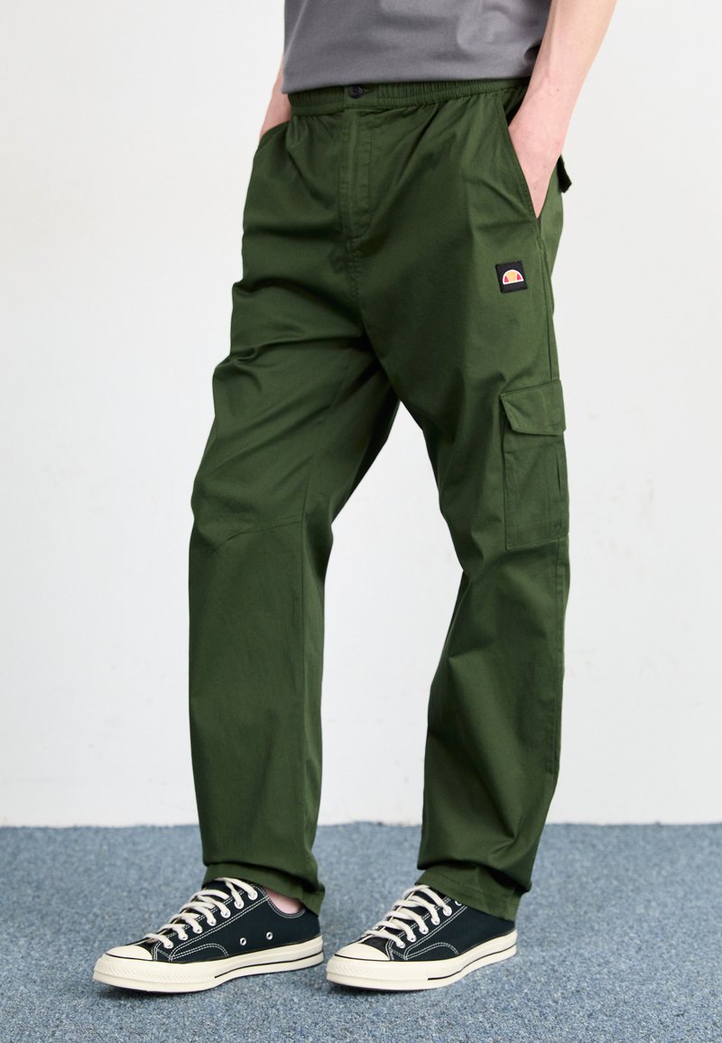 Groene cargobroek van lichtgewicht stof, met een zijzak en een elastische tailleband. Gepaard met zwarte canvas sneakers.