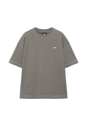 Nadmerné sivé tričko s krátkym rukávom, rebrovaným okrúhlym výstrihom a malým bielym logom na ľavej strane hrudníka na bielom pozadí.