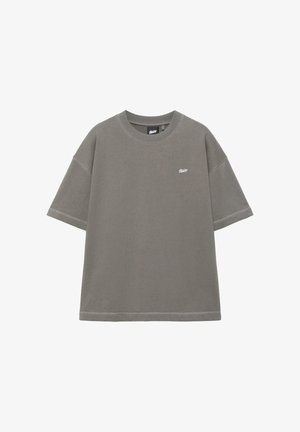 T-shirt gris surdimensionné à manches courtes avec col rond côtelé et petit logo blanc sur la poitrine gauche, sur fond blanc.