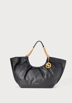 Sort blød læderhåndtaske med guldkædehåndtag, en hængende guldfarvet MK-charm og lille gyldigt "Michael Kors"-logo foran.