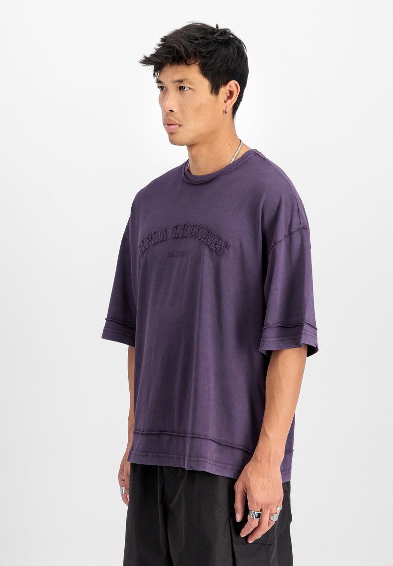 Fialová oversized tričko s krátkymi rukávmi, okrúhlym výstrihom a vyšitým logom "Alpha Industries" na prednej strane. Materiál z bavlneného zmesi.