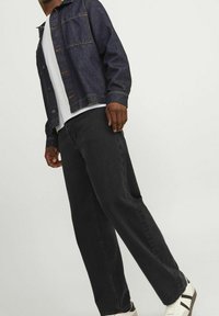 Chaqueta vaquera de color azul oscuro, con costuras naranjas y bolsillos delanteros; combinada con pantalones negros y camiseta blanca; calzado con zapatillas deportivas casuales.