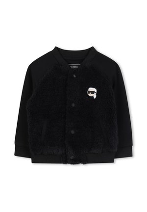 Veste bomber noire avec un devant en fourrure noire duveteuse, des manches en tricot et un col rond. Présente un petit logo de dessin animé sur la poitrine gauche.
