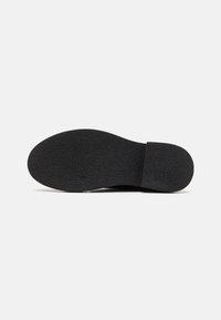 Black shoe sole with a textured surface and a slight heel. Simple, rounded shape, featuring a clean edge at the back.