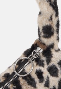 Gros plan sur une fermeture éclair en argent avec une tirette ronde sur un tissu doux à motif léopard avec une texture en fourrure beige, noire et brune.