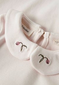 Pale pink top featuring a ribbed texture, round collar with embroidered tulip design, and a back neck closure. Label visible inside collar.