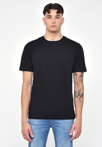 T-shirt nera a maniche corte realizzata in morbido cotone, con scollatura rotonda e un logo discreto sul petto. Abbinata a jeans in denim blu chiaro.