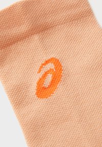 Peach-colored sock made of textured knit fabric featuring a prominent orange logo. The design is simple with a smooth finish.