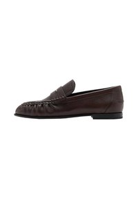 Mocasín de cuero marrón con punta redondeada, detalles cosidos en la parte superior y suela de goma plana. Diseño minimalista y textura suave.