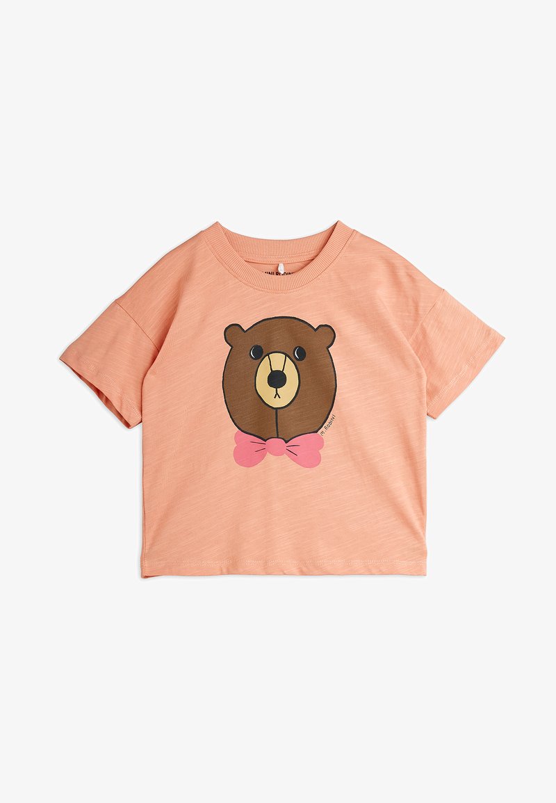 Majica s kratkimi rokavi breskve barve s tiskano risano medvedjo obrazom, ki nosi roza metuljčka spredaj.