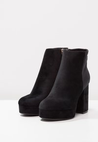 Bottes basses en daim noir avec un talon épais carré et une semelle plateforme. Dotées d'une fermeture éclair latérale et d'une texture lisse.
