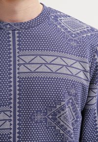 Felpa blu navy con intricati modelli e texture geometriche bianchi, caratterizzata da forme varie tra cui diamanti e strisce.