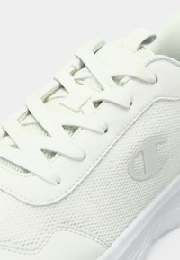 Λευκό αθλητικό παπούτσι με δικτυωτό επάνω μέρος, λείες συνθετικές λεπτομέρειες, επίπεδους κορδόνια και διακριτικό λογότυπο στο πλάι. Στρογγυλερή μύτη και επενδεδυμένη σόλα.