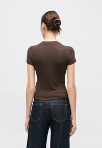 Καφέ κορυφή με κοντά μανίκια από ελαφρύ ύφασμα, με εφαρμοστή σχεδίαση και στρογγυλή λαιμόκοψη, συνδυασμένη με σκούρα μπλε τζιν παντελόνια με φαρδιά πόδια.