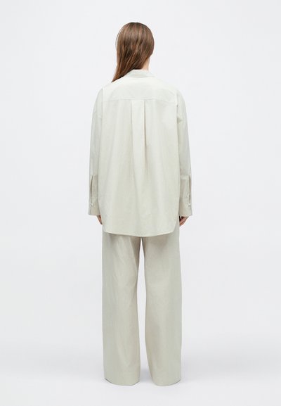 Világos bézs, bő szabású ing és hozzáillő, széles szárú nadrág, texturált anyagból készült. Ing gallérral és gombos mandzsetta r�észletekkel rendelkezik.