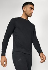 Sort sweatshirt lavet af en bomuldsblanding, med lange ærmer, ribkantede manchetter og bund, samt et diskret logo på den øverste bryst.