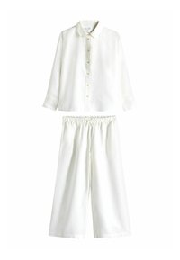 Langärmliges weißes Button-Down-Shirt kombiniert mit lockeren weißen Hosen, die einen elastischen Bund und einen Kordelzug haben.