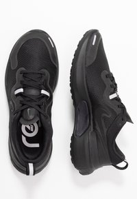 Zapatillas deportivas negras con parte superior de malla, suela de goma, acentos blancos y talón acolchado. Cuenta con cordones y una lengüeta en la parte trasera.