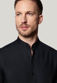 Czarna koszula z kołnierzykiem, wyposażona w zapięcie na guziki, wykonana z gładkiego materiału o subtelnej fakturze, dopasowany krój.