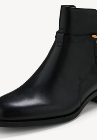 Bottine en cuir noir avec talon bas, détail de bride latérale et bout légèrement pointu, présentée sur un fond neutre.