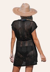 Abito coprente in crochet nero con maniche corte, design a maglia aperta, vita definita e una texture leggera. Abbinato a un cappello di paglia a tesa larga.