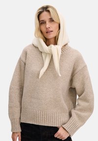 Beżowy sweter dziany z prążkowanym zakończeniem, z okrągłym dekoltem i szerokimi rękawami. Uzupełniony kremowym szalikiem zawiązanym na szyi.