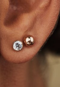 Boucles d'oreilles clous en or rose mettant en vedette une pierre ronde claire en sertisssage clos et une perle sphérique lisse, présentant des surfaces réfléchissantes.