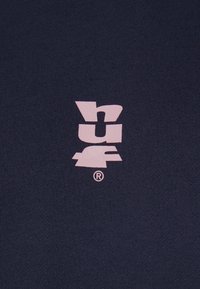 Logo abstrait rose avec des lettres stylisées et un symbole de marque déposée sur un fond de tissu texturé foncé.