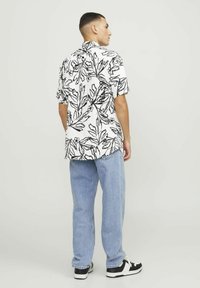 Chemise à manches courtes avec une base blanche et un motif botanique noir. Associée à un jean bleu clair et des baskets noires. Coupe structurée.