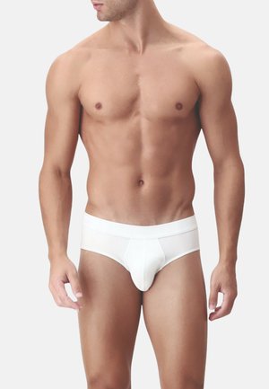 Mutande bianche in cotone con un design aderente, elastico in vita e una borsa sagomata per supporto, esposte su un torso nudo.