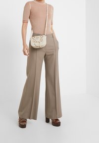 Beige geribbelde top met korte mouwen, hoog getailleerde taupe wijde broek, bruine plateausandalen, crèmekleurige schoudertas met ronde accenten.