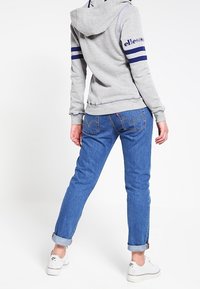 Felpa grigia con righe navy sulle maniche, abbinata a jeans in denim azzurro chiaro arrotolati ai polsi e sneaker bianche.