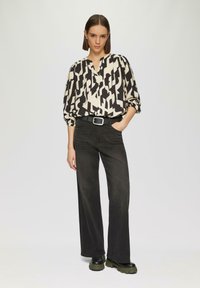 Schwarz-creme gemusterte Bluse mit V-Ausschnitt, kombiniert mit hochgeschnittenen, schwarzen weit geschnittenen Hosen und klobigen schwarzen Plate Stiefeln.
