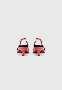 Escarpins en cuir verni rouge avec un talon fin, une bride de cheville réglable et un design à bout ouvert. La semelle noire contraste vivement.