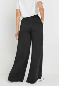 Pantalons larges noirs avec une coupe décontractée, taille élastique et poches. Fabriqués à partir d'un tissu léger, présentant une texture lisse.