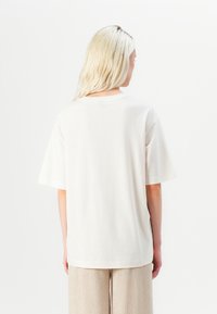 Svetlo béžové oversized tričko s okrúhlym výstrihom a krátkymi rukávmi, vyrobené z mäkkej bavlnenej zmesi, s jednoduchou hladkou textúrou.