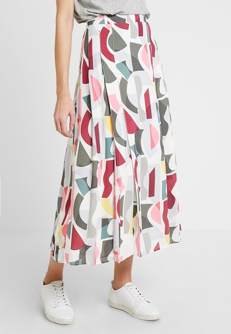 Falda midi plisada en tejido ligero, con un estampado geométrico multicolor que incluye rojos, verdes, amarillos y rosas. Combinada con zapatillas blancas.