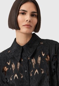 Zwarte kantblouse met bloemen uitsnijdingen, een klassieke kraag, knoopsluiting en textiel met complexe details.