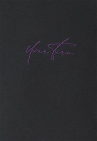 Černá látka s hladkým povrchem, na přední straně s fialovým vyšitým nápisem "Tvůj tah".