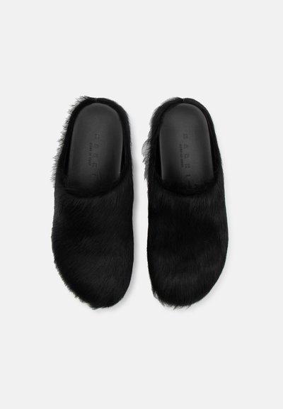 Pantofi slip-on din blană neagră, cu un interior neted și o formă rotundă, având un exterior texturat din blană artificială lungă.