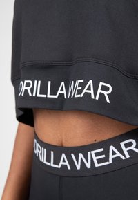 Black cropped sweatshirt with "GORILLA WEAR" logo in white. Paired with black high-waisted leggings featuring a matching logo band.