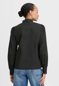 Black long-sleeve shirt featuring a scalloped collar, puffed sleeves, and buttoned cuffs, paired with high-waisted blue jeans.