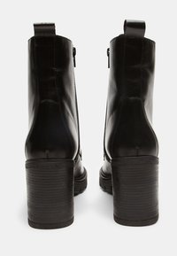 Botine din piele neagră până la gleznă, cu toc masiv, având un fermoar lateral și o buclă în spate pentru un plus de confort la încălțare. Textură netedă.