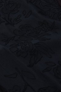 Zwarte stof met een geperst bloemmotief met gedetailleerde accenten. De textuur lijkt glad en licht verhoogd.