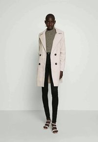 Valkoinen raidallinen turtleneck-paita ruskeaviininpunaisella kaksirivinenn takilla, yhdistetty mustiin kapeisiin farkkuihin ja valkoisiin sandaaleihin.