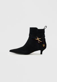 Black suede ankle boot with a pointed toe, decorative strap and gold hardware accent, featuring a low kitten heel and pull tab at the back.