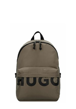 Mochila de tela beige con un acabado texturizado, que presenta un gran logotipo negro "HUGO", doble cremallera, bolsillo frontal y un asa superior.