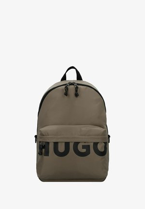 Mochila de tela beige con un acabado texturizado, que presenta un gran logotipo negro "HUGO", doble cremallera, bolsillo frontal y un asa superior.
